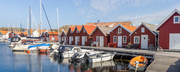 Harbor scene on Tjorn island, Sweden, with falu red wooden houses and moored boats along the pier