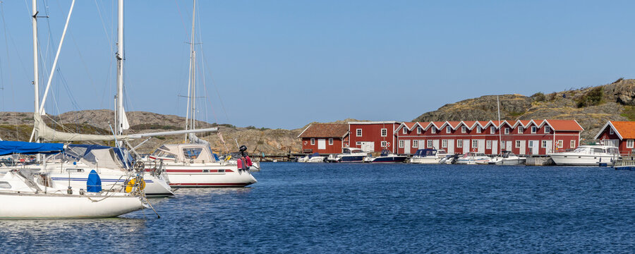 Harbor scene on Tjorn island, Sweden, with falu red wooden houses and moored boats along the pier