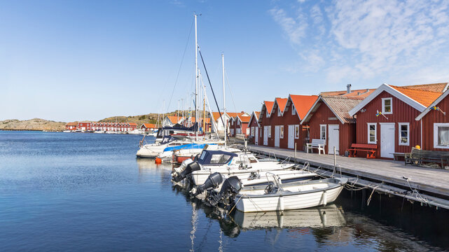Harbor scene on Tjorn island, Sweden, with falu red wooden houses and moored boats along the pier