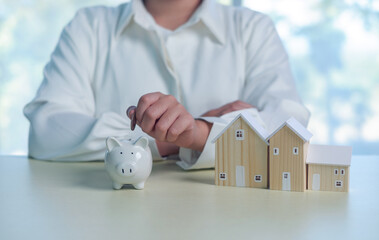 White piggy bank with coin and wooden house models on desk, representing home savings, mortgage...