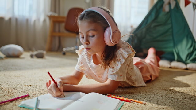 Carefree kid drawing notebook lying carpet. Creative clever child doing homework