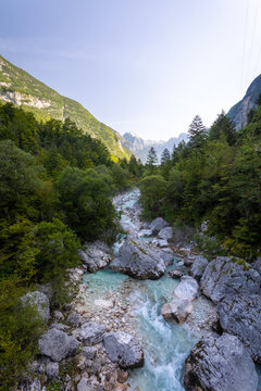 Turquoise Soca Isonzo River flowing through a rocky alpine gorge with clear water, boulders and green forest in Slovenia near Bovec