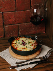 Cheesy baked casserole in cast iron dish with red wine on rustic table