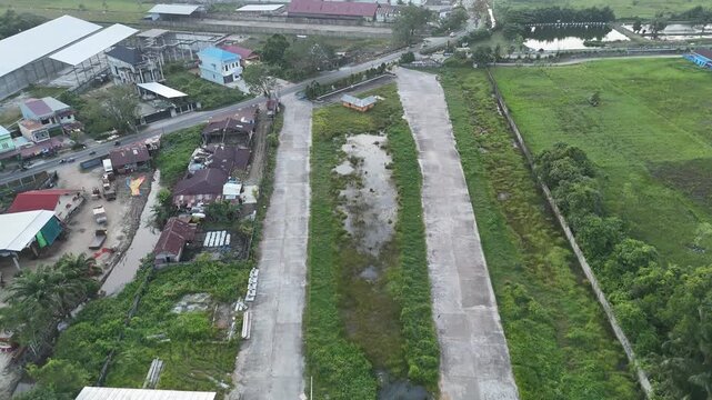 An aerial shot shows a rural community with a central concrete road, lush fields, scattered houses, and light industrial structures, illustrating development amid countryside and open space.