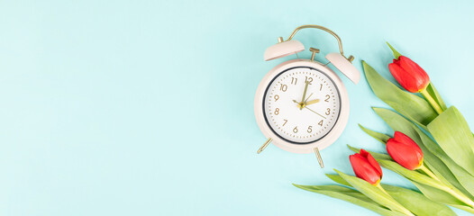 Switch to daylight saving time in spring, summer time changeover, alarm clock with red tulip flowers