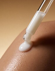 white milk lotion is pouring out of a glass dropper on dark skin, macro texture of the skin on which the lotion is applied