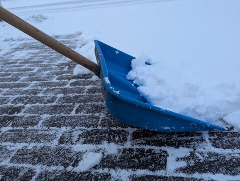 Blue plastic shovel placed on icy pavement surrounded by fresh snow, bold contrast and crisp winter mood ideal for snow removal, cold climate, and seasonal maintenance concepts.