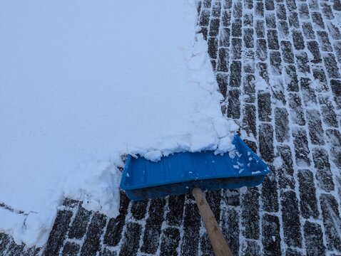 Bright blue plastic snow shovel resting on a snow-covered pavement after snowfall, strong color contrast highlighting winter cleanup, cold weather, and driveway or sidewalk clearing.