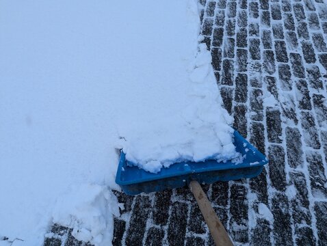 Blue snow shovel resting on snow-covered ground, high contrast winter image representing snowfall aftermath, cleanup work, and preparation for icy conditions.