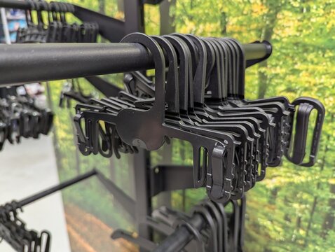 Black plastic clothing hangers lined on a metal retail rail inside a store, vibrant green foliage photo backdrop creating a bright, fresh mood for fashion, storage, and lifestyle branding.
