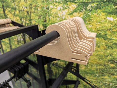 Row of recyclable cardboard hangers on a metal shop rail with lush green foliage print behind, modern and fresh aesthetic suited for sustainable fashion and lifestyle branding.