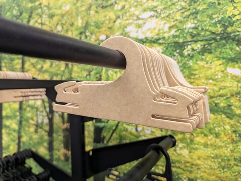 Cardboard clothing hangers lined on a metal retail rail with vibrant green foliage photo backdrop, bright and fresh atmosphere ideal for sustainable fashion, store displays, and lifestyle concepts.