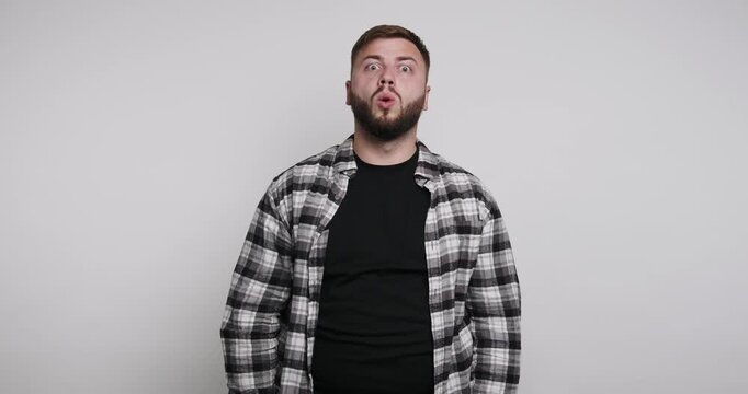 Man shows surprise reaction while standing against plain wall in indoor setting