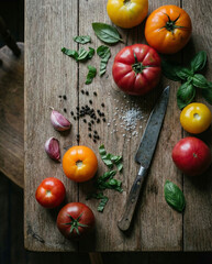 Rustic flatlay of colorful heirloom tomatoes, fresh basil, garlic and vintage knife on wooden table