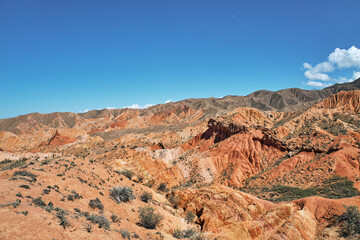 Fototapeta premium Colorful scenic mountain landscape with red and orange rock formations under a bright blue sky. Natural wonder and travel destination concept.