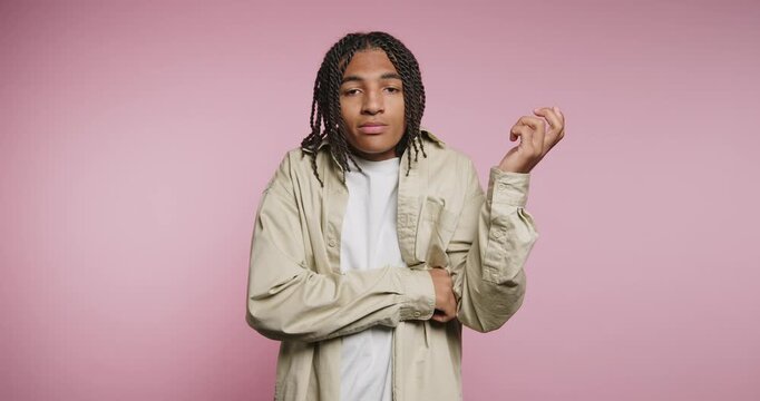 Young individual stands in front of pink backdrop wearing casual clothes with hands crossed