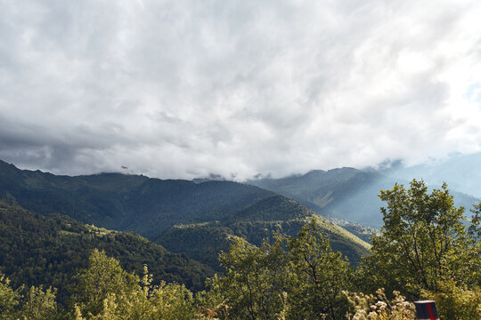 mountains forest clouds landscape mist sky trees hills under dramatic cloudy sky with layered mountain ridges and sunlight - Powered by Adobe