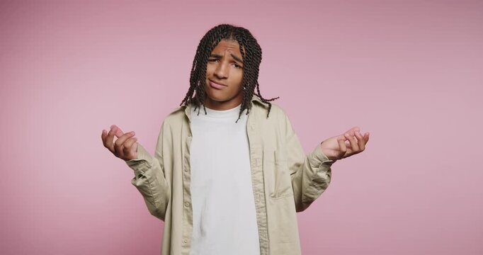 Young man expresses confusion while standing in front of a pink wall in a studio environment