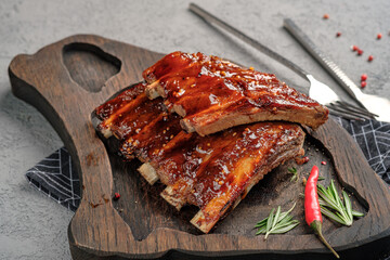 Glazed barbecue pork ribs with sticky sauce, served on rustic wooden board with fresh rosemary and red chili garnish. Juicy grilled spare ribs, gourmet meat dish, appetizing dinner or party food.