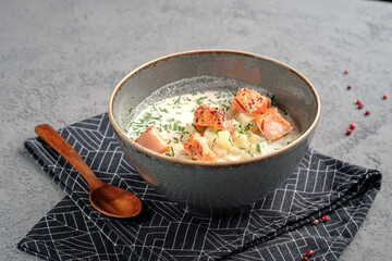 Creamy potato soup topped with seared salmon pieces and chopped herbs in ceramic bowl. Rich Nordic salmon chowder, wholesome seafood meal, restaurant-style presentation.