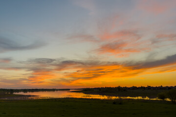 Obraz premium Colorful sunset sky with orange and gold clouds above quiet natural landscape
