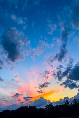 Fototapeta premium Vertical sunset sky with glowing horizon and clouds above dark landscape