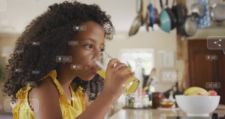 Sipping girl wearing yellow ruffled top at kitchen counter, holding clear glass of orange juice