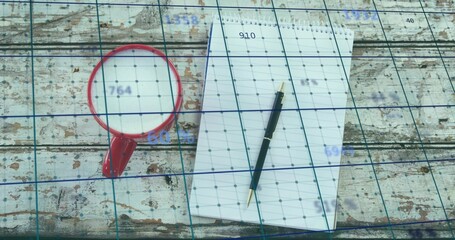 Resting spiral notepad with black ballpoint pen on worn wooden table, red mug and blue grid