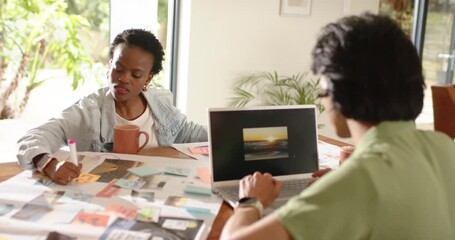 Diverse coworkers scrolling laptop then writing sticky notes refining ideas in sunlit workspace