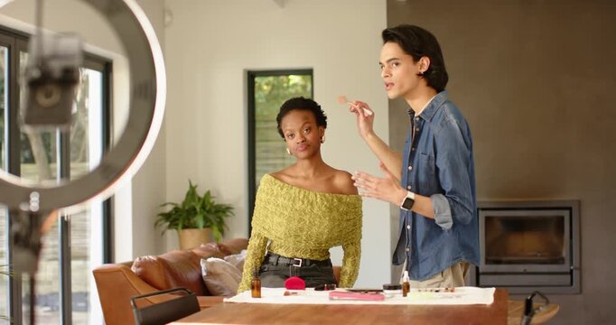 Male makeup artist picking powder applying it to African American female model for tutorial at home
