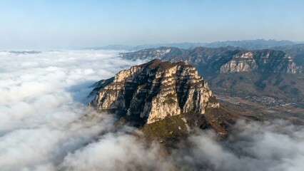 Obraz premium Aerial view of a rugged mountain peak rising above a sea of clouds with distant mountain ranges under a clear sky