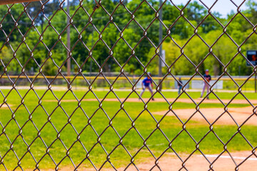 Selective focus on a chain link fence at a youth baseball game blurred in the background.