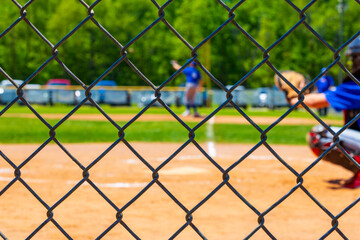 Selective focus on a chain link fence at a youth baseball game blurred in the background.
