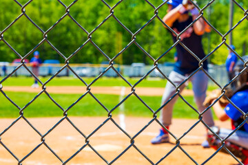 Selective focus on a chain link fence at a youth baseball game blurred in the background.