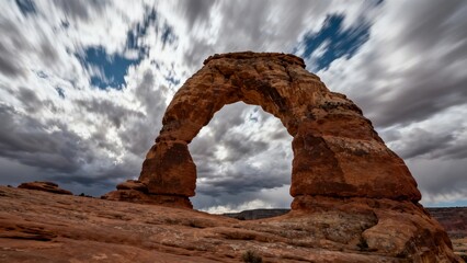 A large natural sandstone arch under a dramatic cloudy sky in a desert landscape