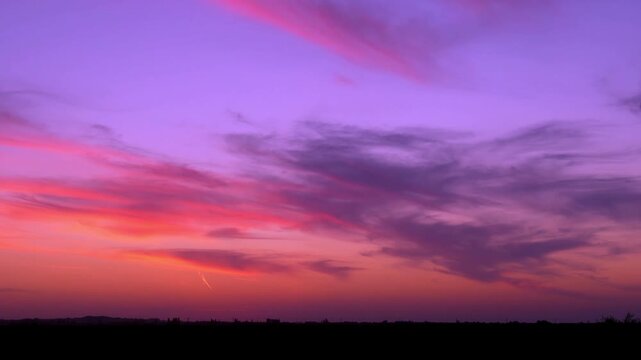 Amazing colorful dawn over a field a bright colored sky sun and light feathery clouds fast time lapse horizon. Sun beautiful sky and cirrus clouds changing colors and a meadow, time-lapsed landscape.