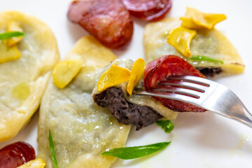 Gourmet Ukrainian pierogi, filled with black beans and served with fried garlic and grilled sausage, garnished with sliced ​​fresh scallions.
