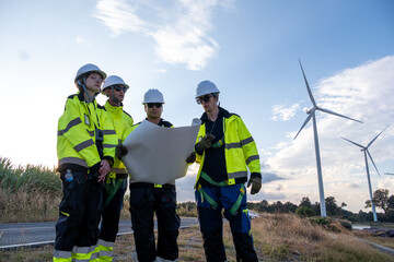 Fototapeta premium Group of workers inspecting plans at a wind farm site in the afternoon sun near tall wind turbines
