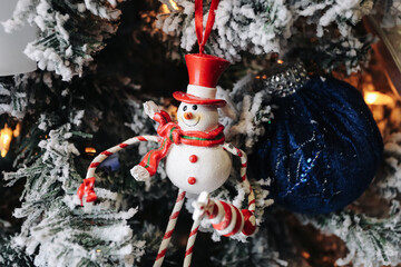 Snowman Christmas tree ornament closeup. Red hat and scarf decoration. Winter holiday interior detail with lights. Festive seasonal atmosphere at home. Cozy winter celebration scene.