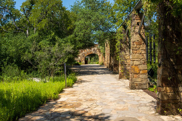 A stone pathway leads to an archway in Lady Bird Johnson wildlife center in Austin Texas Lush greenery and trees surround the path © steheap