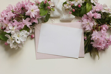 Blank paper greeting card, pink envelope, surrounded by Japanese cherry blossoms, apple flowers, silk ribbon. Beuatiful floral mockup for wedding invitations, stationery, greetings, or spring messages