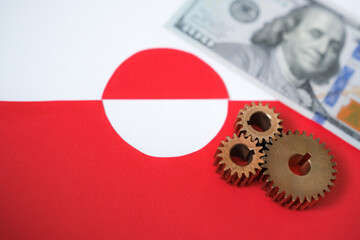 Metal gears on a blurred background of the flag of Greenland and United States dollars. Geopolitical interests in the Arctic region. Abstract political concept.