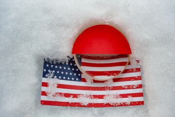 Metaphorical look at the relationship between America and Greenland. Exaggeration and unknown developments. Symbol of countries and a magnifying glass on a snowy surface.