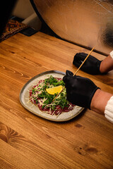 Hands in black rubber gloves adjust a dish in a restaurant