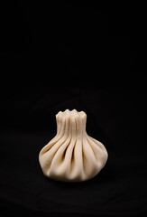 One handmade khinkali on a black background