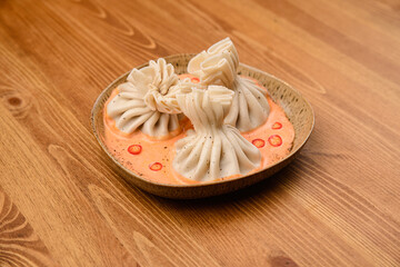 A plate with three khinkali in tomato-cream sauce
