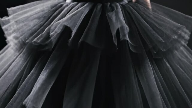A young dancer mesmerizes with her delicate movements while wearing a stunning black tulle dress. The setting is dimly lit, highlighting her form. The atmosphere feels magical and artistic.