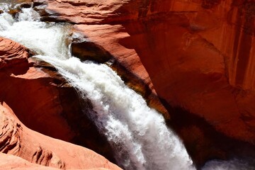 Waterfall cascading through red rock canyon with rushing white water and rugged sandstone formations