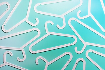 White Plastic hangers as minimal pattern on teal gradient background, Clothes rack for organizing clothes in closets or retail stores for hanging of garments, top view, fashion, organization content