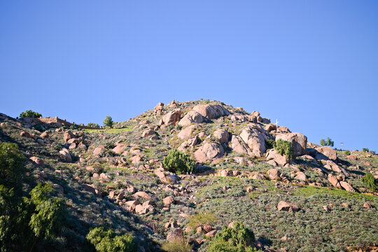Rocky hillside on Mount Rubidoux in Riverside, California, covered with chaparral and boulders beneath a clear blue sky.
